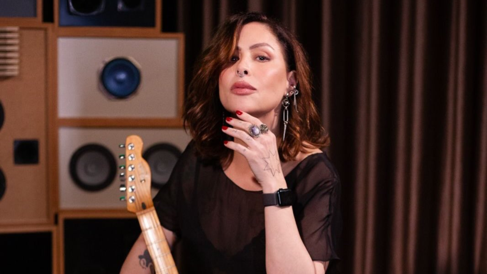 A cantora Pitty segurando uma guitarra em estúdio, diante de caixas amplificadoras
