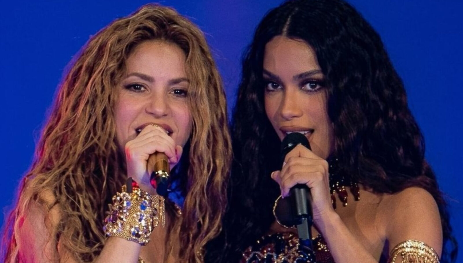 Shakira e Anitta cantando juntas ao microfone em um palco