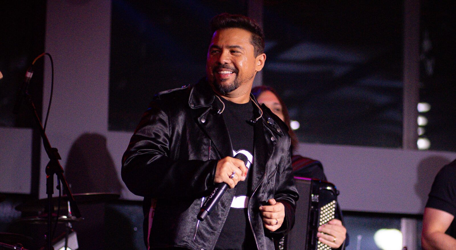 O cantor Xand Avião sorrindo com microfone na mão durante show