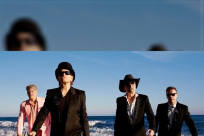 Os quatro integrantes do U2 caminham de terno na beira do mar, com ondas ao fundo